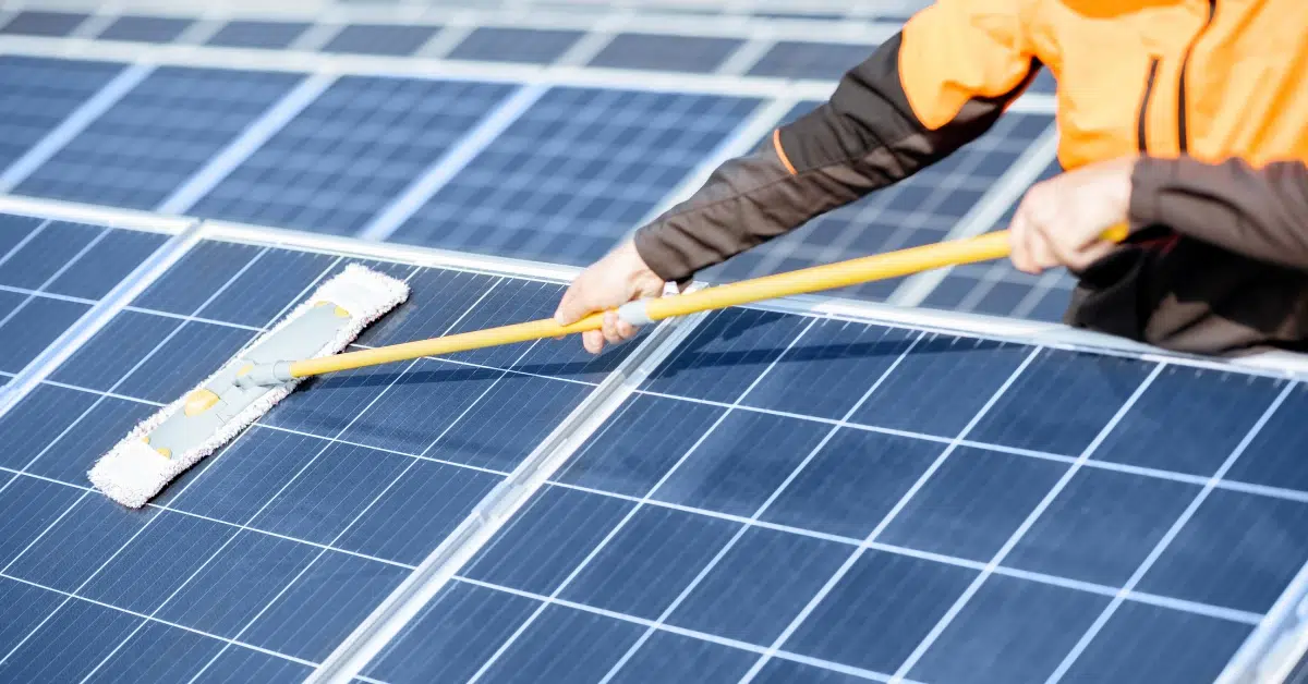 a worker in an orange jacket cleans solar panels - best practices for solar panel maintenance